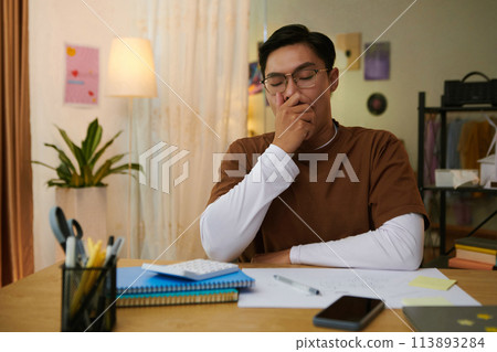 High school student bored of doing homework, he is yawning and covering mouth with hand 113893284