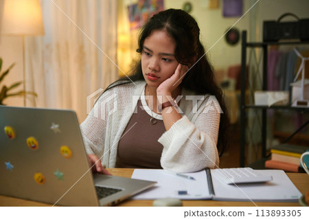 Portrait of pensive girl reading math students book on laptop when doing homework 113893305