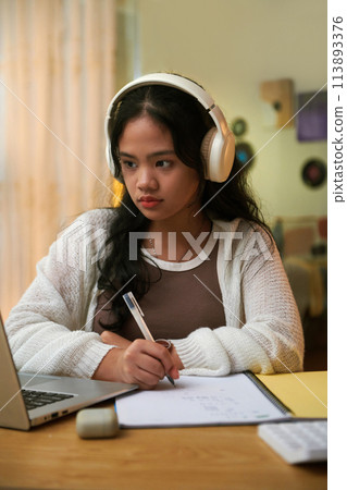 Portrait of schoolgirl watching educational video and writing down main ideas Portrait of schoolgirl watching educational video and writing down main ideas 113893376