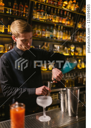 Bartender measures blue syrup for cocktail using jigger 113894085