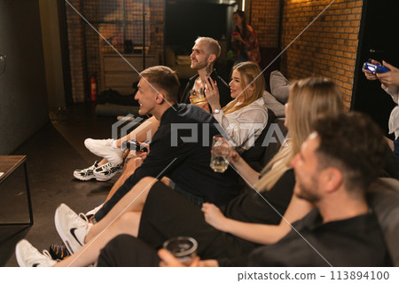 Group of gamers assembles around screens to play on console Group of gamers assembles around screens to play on console 113894100