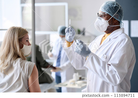 Side view portrait of senior doctor wearing mask holding syringe during mass vaccination in clinic copy space Side view portrait of senior doctor wearing mask holding syringe during mass vaccination in clinic copy space 113894711
