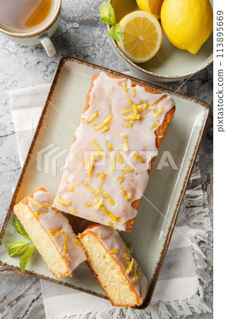 Lemon Drizzle Cake is a classic British cake known for its moist texture and vibrant lemon flavour closeup on the plate. Vertical top view 113895669