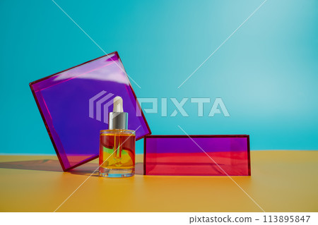 yellow face oil in glass bottle with dropper on yellow and blue background with pink and purple geometric elements. Bright fun minimalist summer skincare concept yellow face oil in glass bottle with dropper on yellow and blue background with pink and purple geometric elements. Bright fun minimalist summer skincare concept 113895847