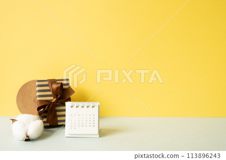 Gift box and calendar on gray table. yellow wall background Gift box and calendar on gray table. yellow wall background 113896243
