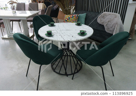 White wooden table complete with green wooden chairs with soft fabric upholstery. Green cups on the table 113896925