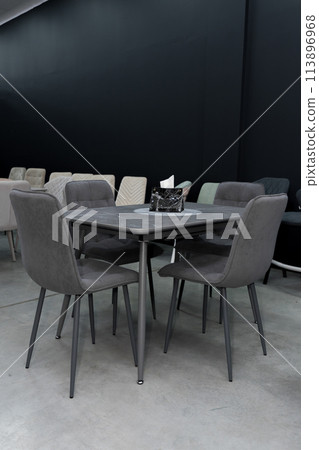 Gray wooden table combined with dark gray wooden chairs with soft fabric upholstery. There is a black napkin holder on the table Gray wooden table combined with dark gray wooden chairs with soft fabric upholstery. There is a black napkin holder on the table 113896968