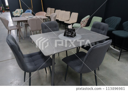 Gray wooden table combined with dark gray wooden chairs with soft fabric upholstery. There is a black napkin holder on the table Gray wooden table combined with dark gray wooden chairs with soft fabric upholstery. There is a black napkin holder on the table 113896981