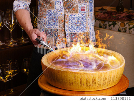 Flambe cheese wheel pasta preparation 113898151
