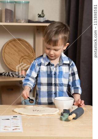 Little child sprinkling dough with flax seeds, making cookies in the kitchen. Little child sprinkling dough with flax seeds, making cookies in the kitchen. 113898581