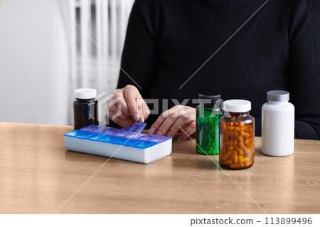 Female putting prescription pills and vitamins in a daily pill box organizer. Sorting nutritional supplements and antibiotics into weekly pills container. 113899496