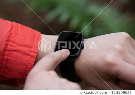 Close-up view of a woman using her smart watch in nature 113899625