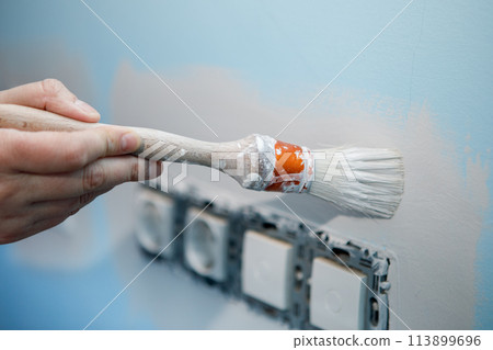 Preparation work to paint the wall of the house, edging the sockets before rolling the roller 113899696