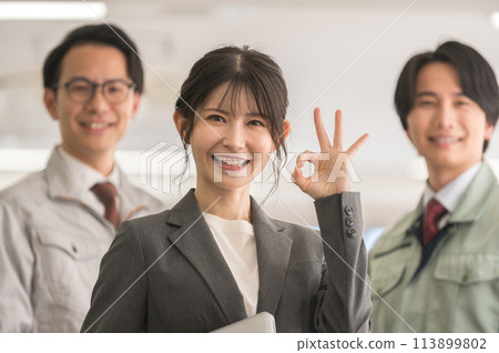 A woman in a suit and a male engineer in work clothes posing OK while holding a laptop 113899802