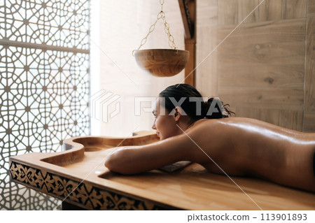 Beautiful young woman lying on spa bed for wellness treatment at spa resort on vacation. Satisfied carefree woman enjoying leisure in beauty parlor. Concept of healthy lifestyle and body care. 113901893