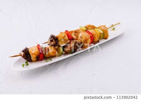 Grilled chicken skewers with vegetables on white plate 113902042