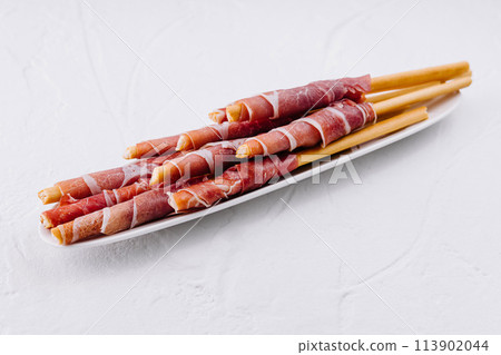Gourmet prosciutto wrapped breadsticks on plate 113902044
