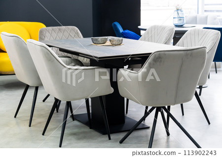 Gray wooden table combined with gray chairs with soft fabric upholstery. There is a black porcelain plate on the table 113902243