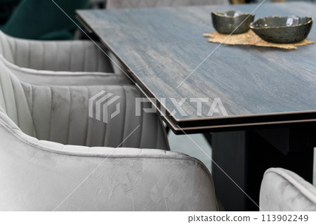 Gray wooden table combined with gray chairs with soft fabric upholstery. There is a black porcelain plate on the table 113902249