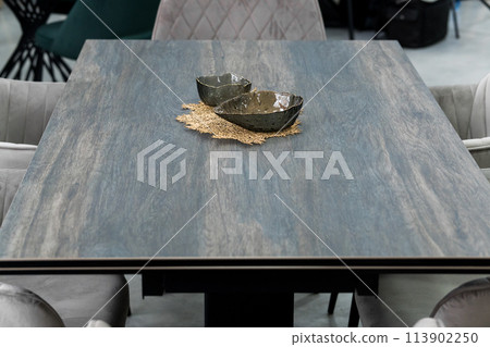 Gray wooden table combined with gray chairs with soft fabric upholstery. There is a black porcelain plate on the table Gray wooden table combined with gray chairs with soft fabric upholstery. There is a black porcelain plate on the table 113902250