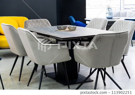 Gray wooden table combined with gray chairs with soft fabric upholstery. There is a black porcelain plate on the table 113902251
