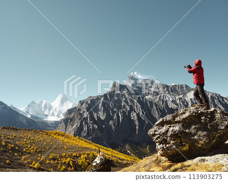 asian photographer standing on top of rock taking photo of Mount Yangmaiyong (or Jampayang in Tibetan) in Yading, China 113903275