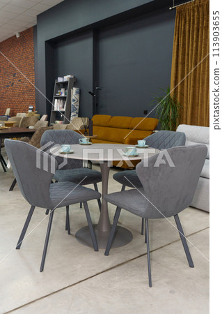 Gray wooden table combined with dark gray wooden chairs with soft fabric upholstery. There are blue porcelain mugs and saucers on the table Gray wooden table combined with dark gray wooden chairs with soft fabric upholstery. There are blue porcelain mugs and saucers on the table 113903655
