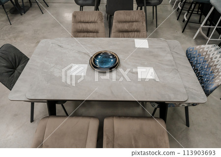 Gray wooden table combined with beige wooden chairs with soft fabric upholstery. Blue and black porcelain plates on the table Gray wooden table combined with beige wooden chairs with soft fabric upholstery. Blue and black porcelain plates on the table 113903693