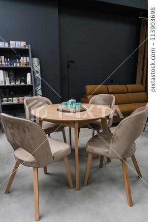 A yellow wooden table combined with beige wooden chairs with soft fabric upholstery. There is a porcelain teapot and blue mugs on the table A yellow wooden table combined with beige wooden chairs with soft fabric upholstery. There is a porcelain teapot and blue mugs on the table 113903698