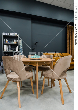 A yellow wooden table combined with beige wooden chairs with soft fabric upholstery. There is a porcelain teapot and blue mugs on the table A yellow wooden table combined with beige wooden chairs with soft fabric upholstery. There is a porcelain teapot and blue mugs on the table 113903710