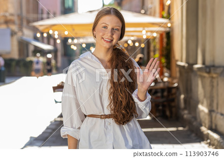 Young girl smiling friendly at camera, waving hands hello, hi, greeting or goodbye in city street Young girl smiling friendly at camera, waving hands hello, hi, greeting or goodbye in city street 113903746