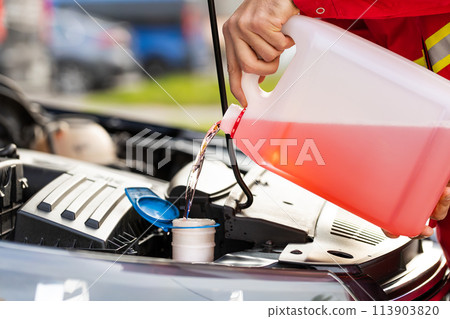 Service worker man pours car fluid windscreen red cleaning washer glass summer or winter cleaner Service worker man pours car fluid windscreen red cleaning washer glass summer or winter cleaner 113903820