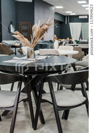 Black wooden table complete with black wooden chairs with soft gray fabric upholstery. Glass vase on the table Black wooden table complete with black wooden chairs with soft gray fabric upholstery. Glass vase on the table 113904623
