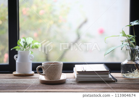 Coffee in a white cup and notebooks on wooden table with plants Coffee in a white cup and notebooks on wooden table with plants 113904674