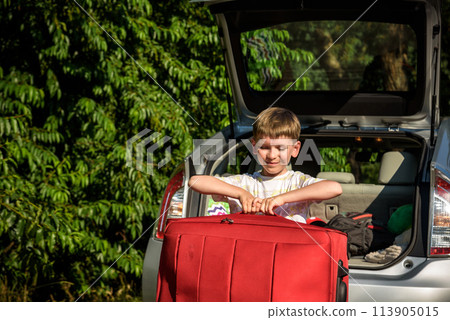 Pretty boy loading the luggage in the trunk of the car. Kid looking forward for a road trip or travel. Family travel by car Pretty boy loading the luggage in the trunk of the car. Kid looking forward for a road trip or travel. Family travel by car 113905015