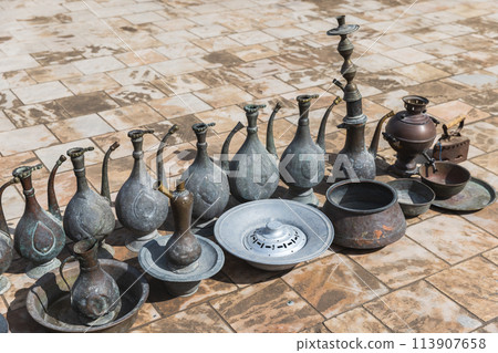 Ancient jugs and other dishes for sale stand on the pavement 113907658