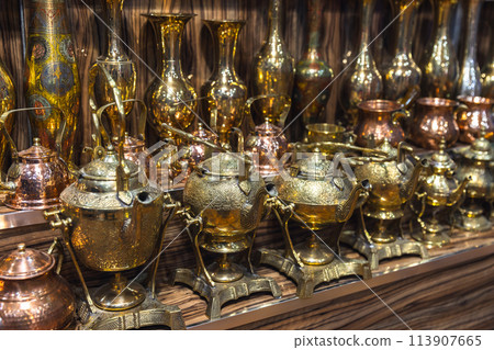 Vintage kettles and vases  with embossed patterns stand in rows 113907665