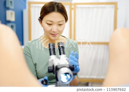 Gynecologist examines a patient using microscope in a gynecological chair. Doctor performs a colposcopy on a young girl in a modern medical office. Diagnosis of cervical cancer. 113907682