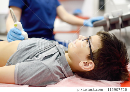 Doctor making abdominal ultrasound for boy using scanner machine. Female doc runs ultrasound sensor over patient tummy. 113907726