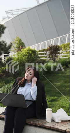 Young happy caucasian business woman or student talking having hybrid work meeting, online class, giving presentation or webinar using laptop computer online technology sitting in city park. 113908022
