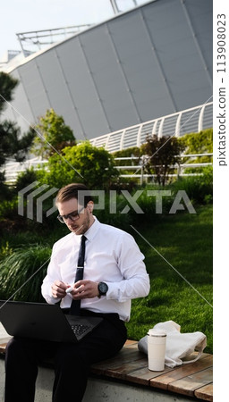 male freelancer working remotely online with headphones and laptop video call conference or distances meeting Male in city park on a bench a modern urban background, outside, outdoors male freelancer working remotely online with headphones and laptop video call conference or distances meeting Male in city park on a bench a modern urban background, outside, outdoors 113908023