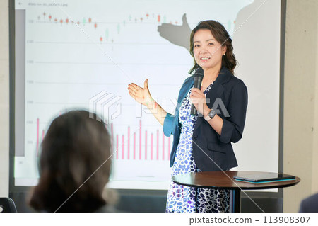Middle-aged female seminar lecturer giving a lecture Middle-aged female seminar lecturer giving a lecture 113908307
