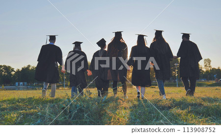 Graduate students walking through an evening meadow at sunset. Graduate students walking through an evening meadow at sunset. 113908752