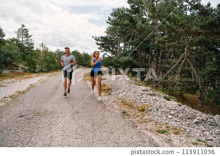 A couple dressed in sportswear runs along a scenic road during an early morning workout, enjoying the fresh air and maintaining a healthy lifestyle 113911036