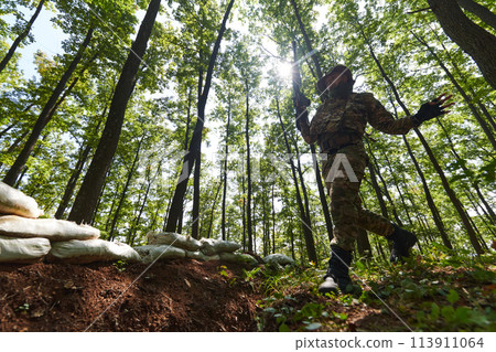 An elite soldier adeptly clears military barriers in the perilous wooded terrain, showcasing tactical skill and agility during specialized training An elite soldier adeptly clears military barriers in the perilous wooded terrain, showcasing tactical skill and agility during specialized training 113911064