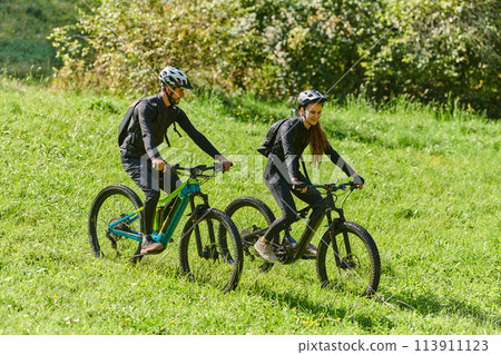 A blissful couple, adorned in professional cycling gear, enjoys a romantic bicycle ride through a park, surrounded by modern natural attractions, radiating love and happiness A blissful couple, adorned in professional cycling gear, enjoys a romantic bicycle ride through a park, surrounded by modern natural attractions, radiating love and happiness 113911123