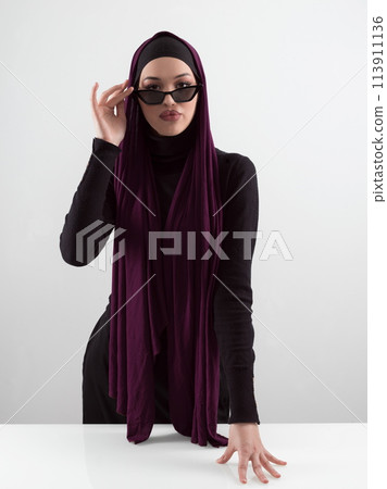 Portrait of beautiful stylish young muslim woman wearing black hijab and sunglasses as modern eastern fashion concept posing on white background. Portrait of beautiful stylish young muslim woman wearing black hijab and sunglasses as modern eastern fashion concept posing on white background. 113911136