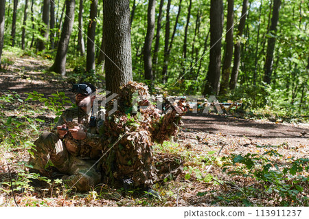 A skilled sniper and a soldier operating a drone with VR goggles strategize and observe the military action while concealed in the forest 113911237