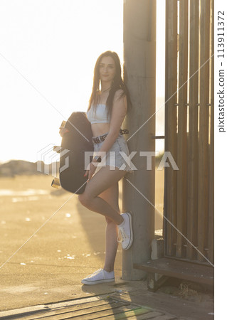 A woman is holding a skateboard and standing next to a fence 113911372