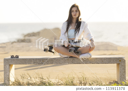 A woman is sitting on a bench with a skateboard in her hand 113911378